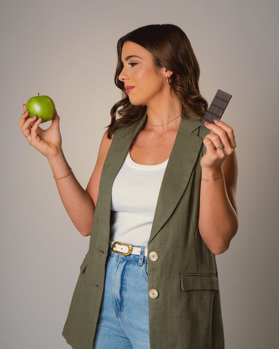 Isabela segurando uma maçã verde numa mão e uma barra de chocolate na outra